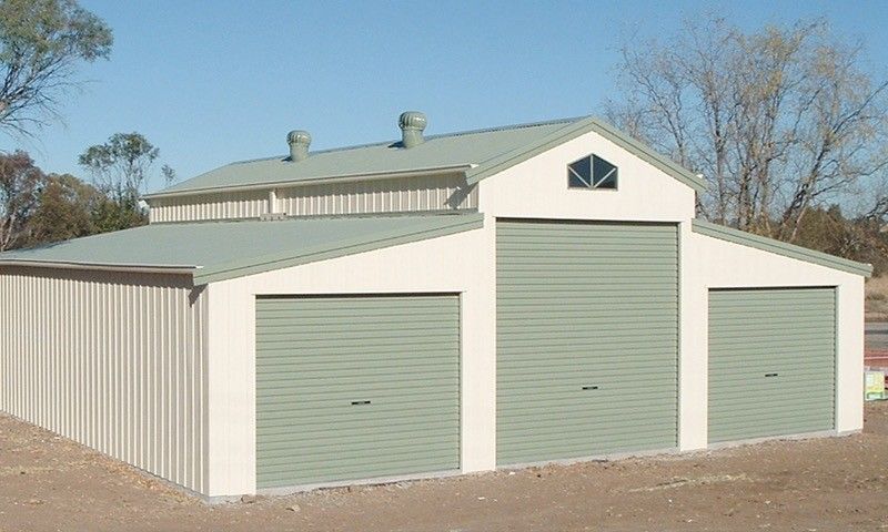 Green and beige metal shed with three garage doors and a loft under a blue sky.