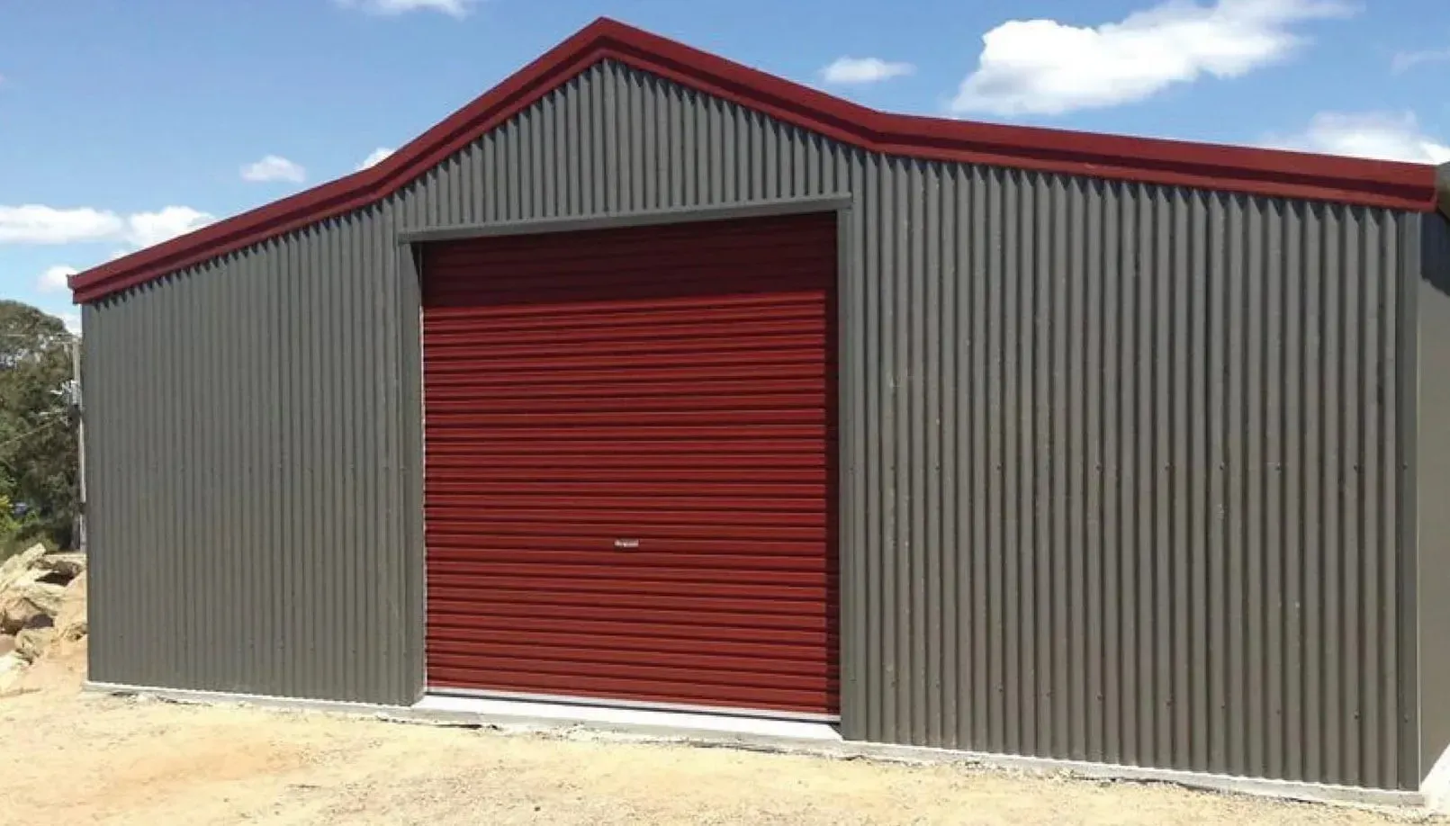 Gray metal shed with red trim and a red roll-up door against a blue sky.