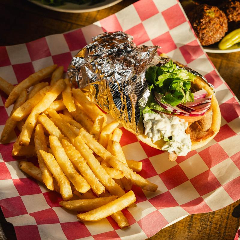 A gyro sandwich wrapped in foil and served with a side of golden french fries on a red and white checkered liner.