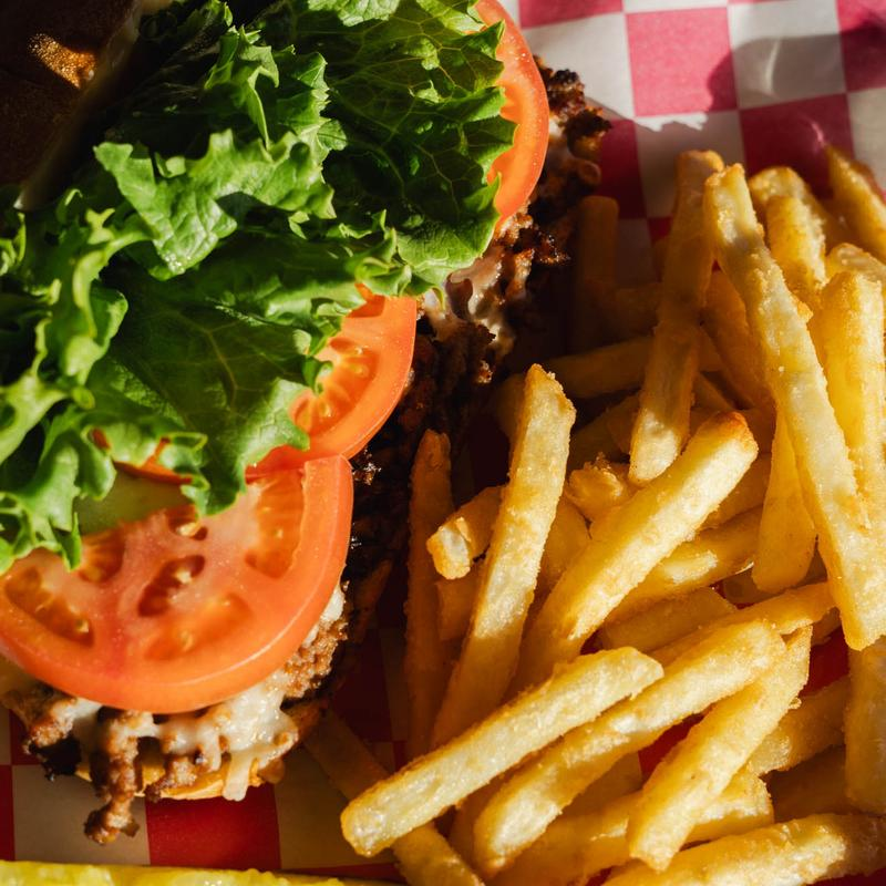 A burger with lettuce and tomatoes next to a pile of golden-brown french fries on a red and white checkered paper liner.