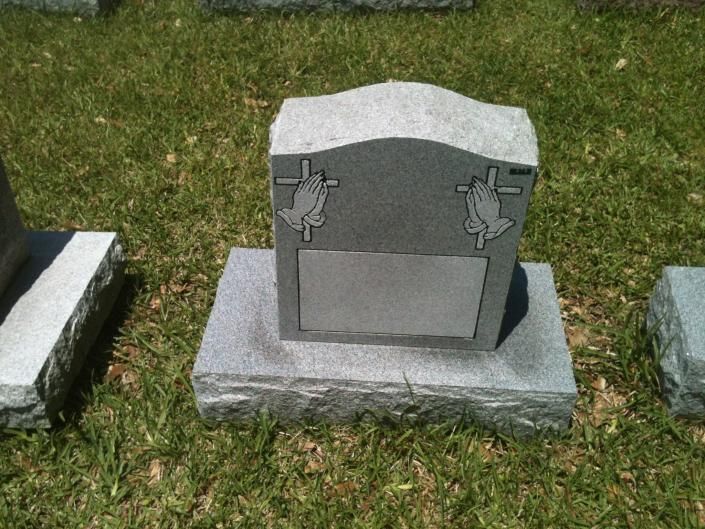 Gray granite gravestone with a blank plaque, flanked by grass and two neighboring headstones.