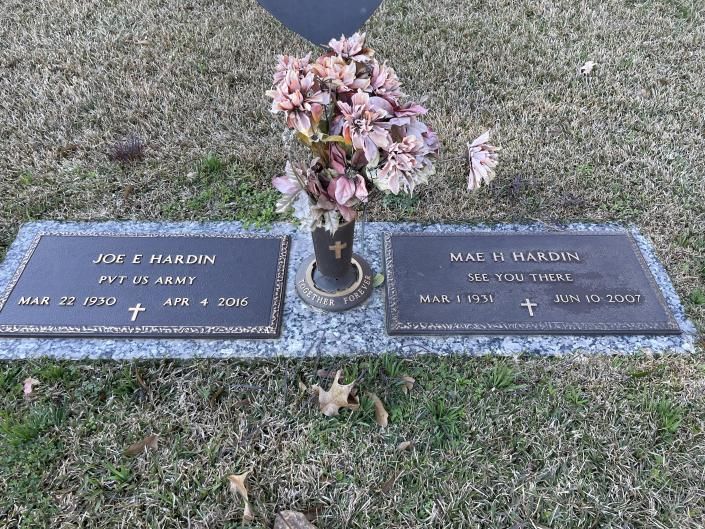 Gravestone with two plaques and pink flowers on grass in a cemetery