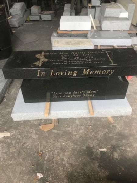 Black memorial grave marker engraved “In Loving Memory,” set on a concrete base indoors