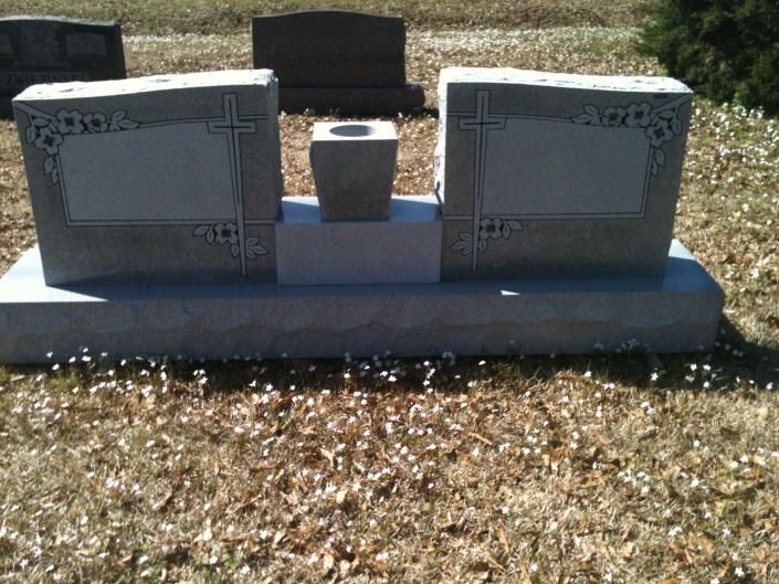 Two gray engraved grave markers with a flower vase on a stone base in a cemetery