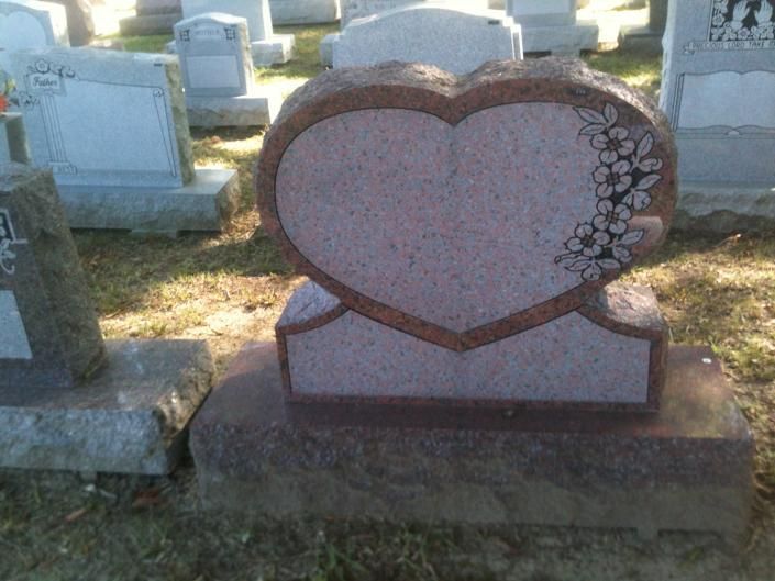 Heart-shaped pink gravestone in a cemetery with floral decoration on the right side