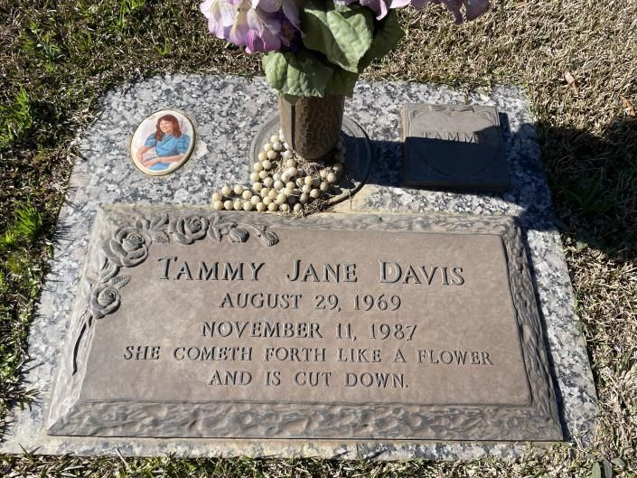 Gravestone for Tammy Jane Davis with flowers and a small photo oval in a cemetery.