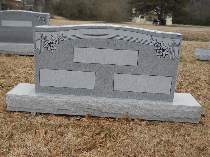 Gray engraved gravestone monument on a lawn, with decorative corners and blank name plates.