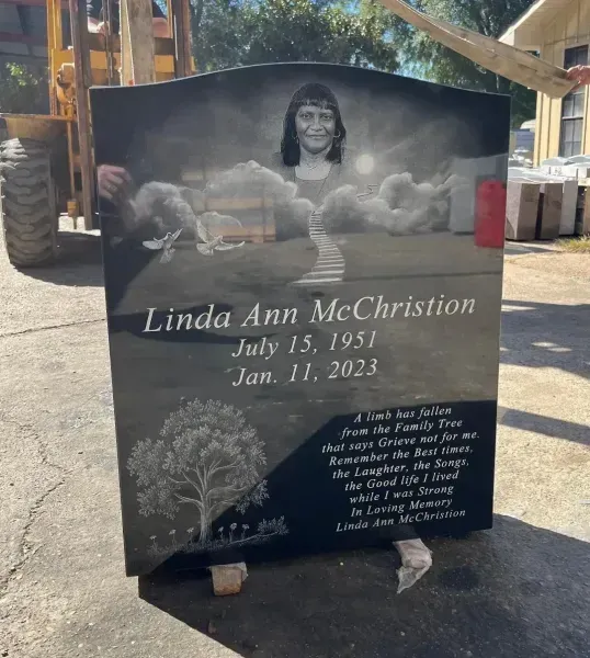 Memorial headstone with portrait and engraved name, set outdoors in a cemetery.
