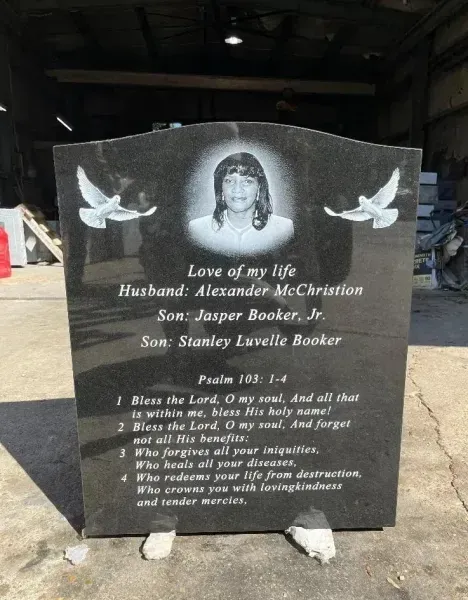 Black funeral memorial stone with a woman’s portrait, doves, and engraved remembrance text.