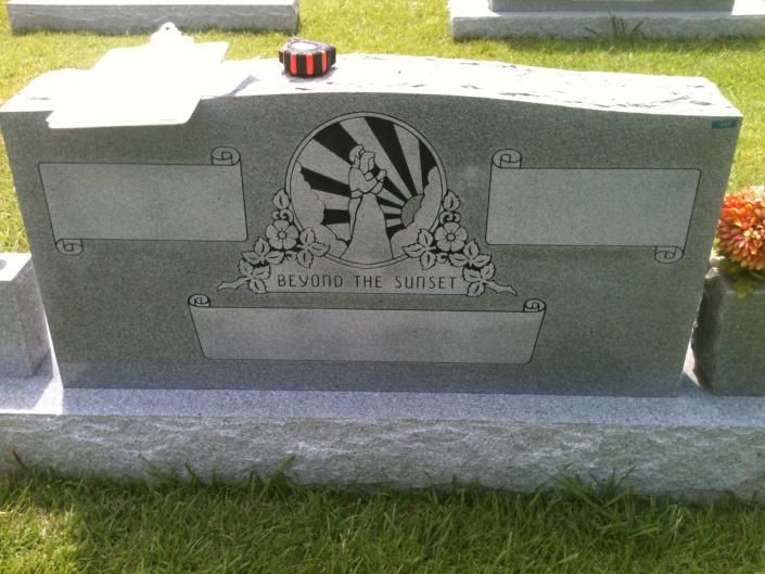 Gray granite gravestone with engraved eagle emblem and plaques, set on a grassy lawn.