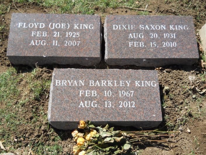 Three engraved memorial bricks in soil, two on top and one below, with flowers at the base.