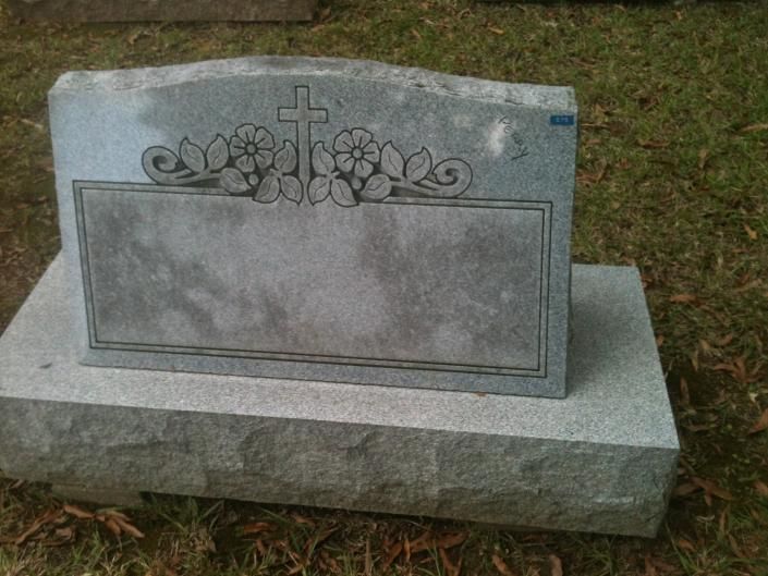 Gray granite gravestone with cross and floral engraving on a grassy cemetery plot