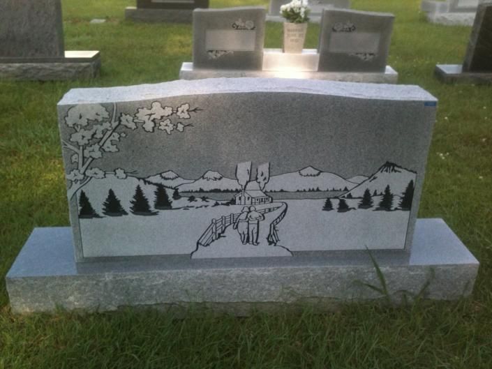 Gray tombstone with etched mountains, trees, stars, and a deer in a snowy landscape