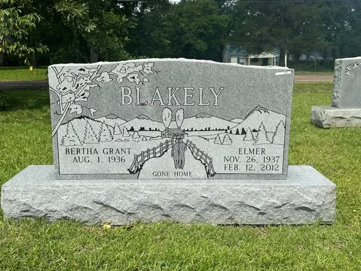 Gray granite memorial headstone in a grassy cemetery, engraved with the name 
