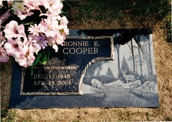Gravestone for Ronnie E. Cooper with engraved trees and pink flowers laid across it.