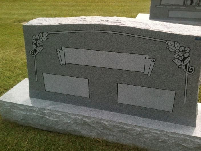 Gray granite gravestone with floral carvings and blank name plaques on a grassy lawn
