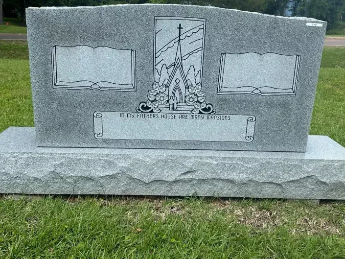 Gray granite gravestone with engraved panels and a central religious monument on a grassy lawn.