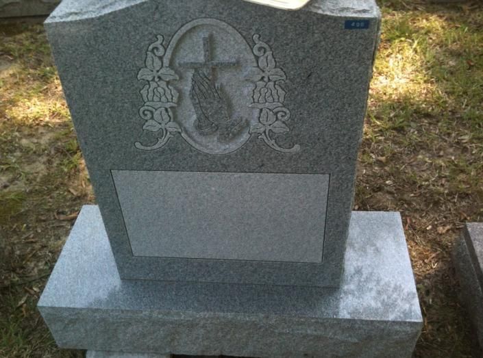 Gray granite gravestone with an engraved cross and floral wreath, set on a cemetery base.