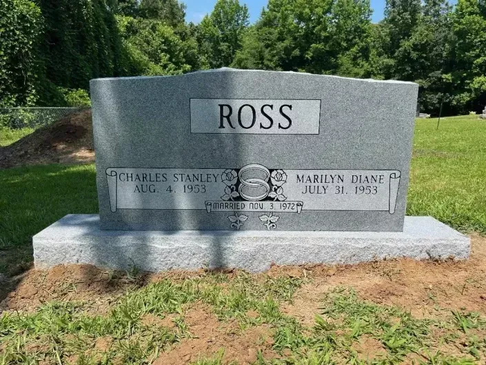 Gray granite memorial marker with “ROSS” engraved, set in a grassy cemetery under trees.