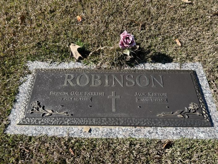 Gravestone in grass with the name Robinson and a small purple flower resting above it.