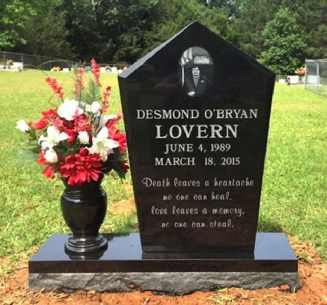 Black gravestone with red-white flowers in a grassy cemetery, engraved “Desmond O’Bryan Lovern.”