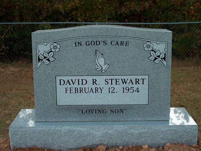 Gray gravestone reading “David R. Stewart, February 12, 1954,” with “In God’s Care” and “Loving Son” engraved.