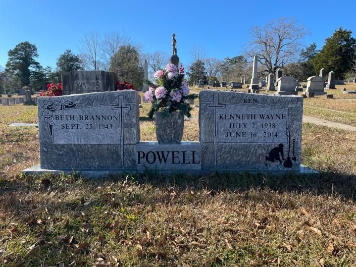 Two gray gravestones with flowers in a cemetery, marked POWELL, under a clear blue sky