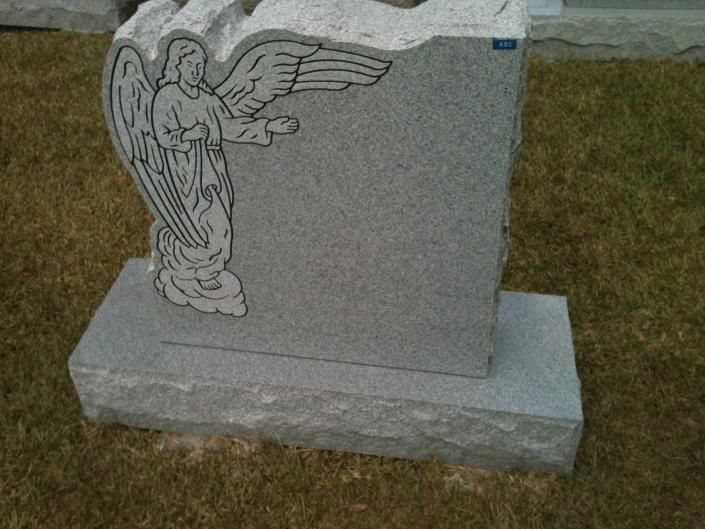 Gray gravestone with an engraved winged angel on a grassy lawn