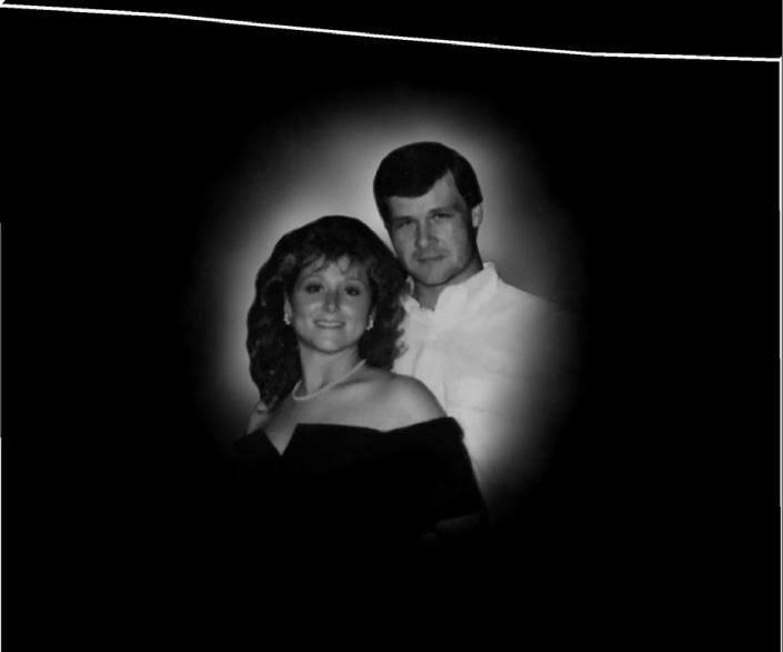 Black-and-white portrait of a smiling couple posed against a dark background.