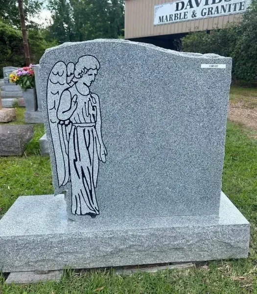 Gray granite gravestone with engraved angel in a cemetery, set on a stone base