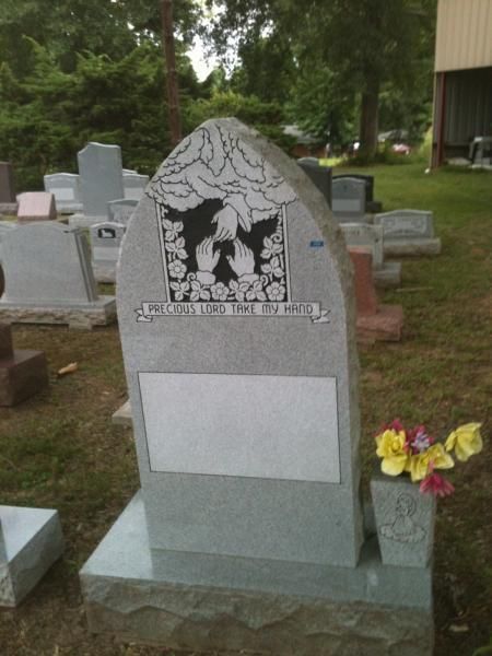 Gray gravestone with etched silhouette, in a cemetery with flowers at the base.