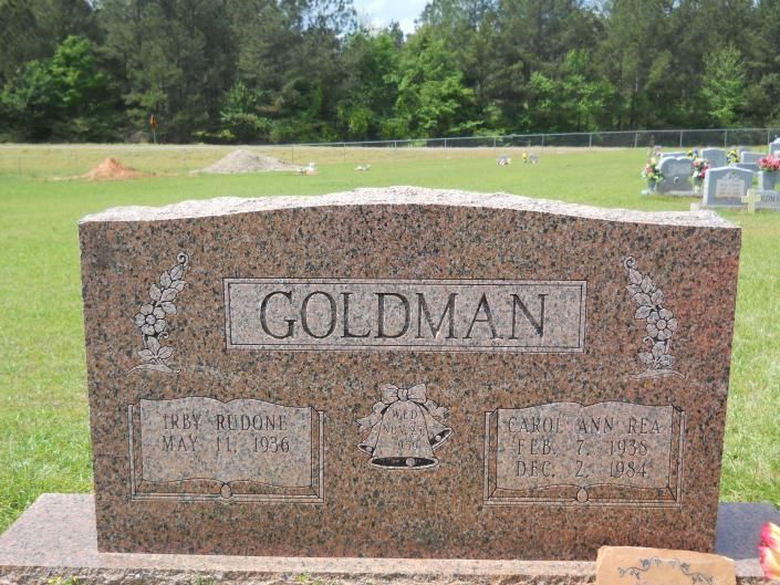 Goldman granite gravestone in a grassy cemetery, with trees in the background.