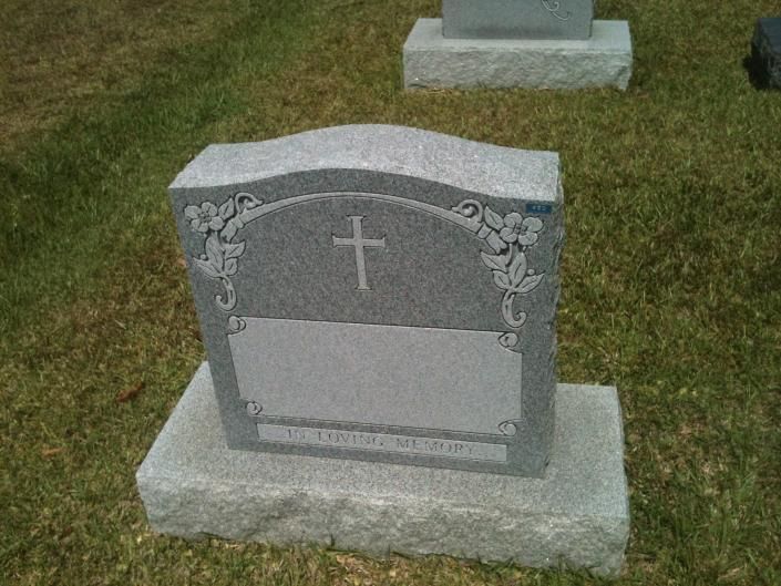 Gray gravestone with a cross and floral carvings on a grassy cemetery plot