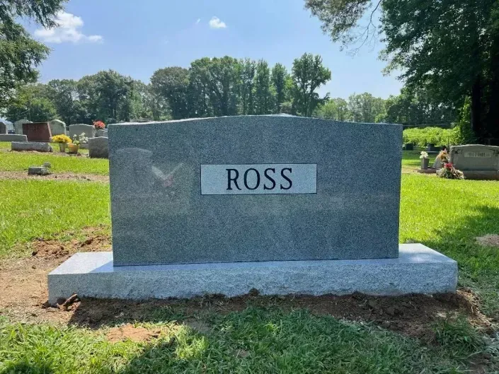 Gravestone marked “ROSS” in a sunny cemetery with grass and trees in the background
