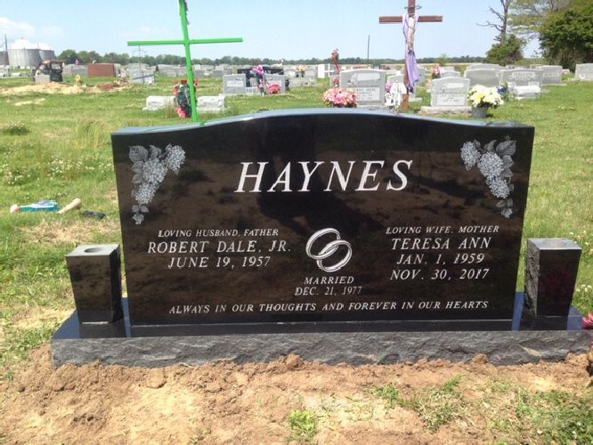 Haynes family gravestone in a cemetery, with black stone cross monument and flowers nearby