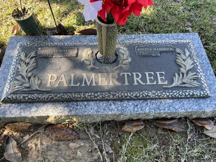 Granite memorial plaque engraved “PALMER TREE” with red flowers in a vase on top
