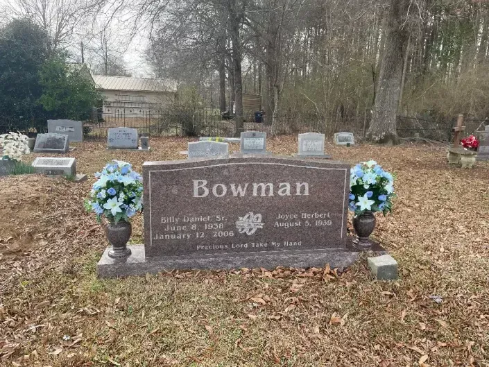 Bowman family gravestone with blue floral arrangements in a wooded cemetery