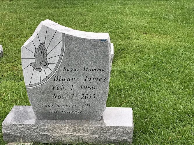 Broken gray gravestone with cracked angel engraving on a green lawn.