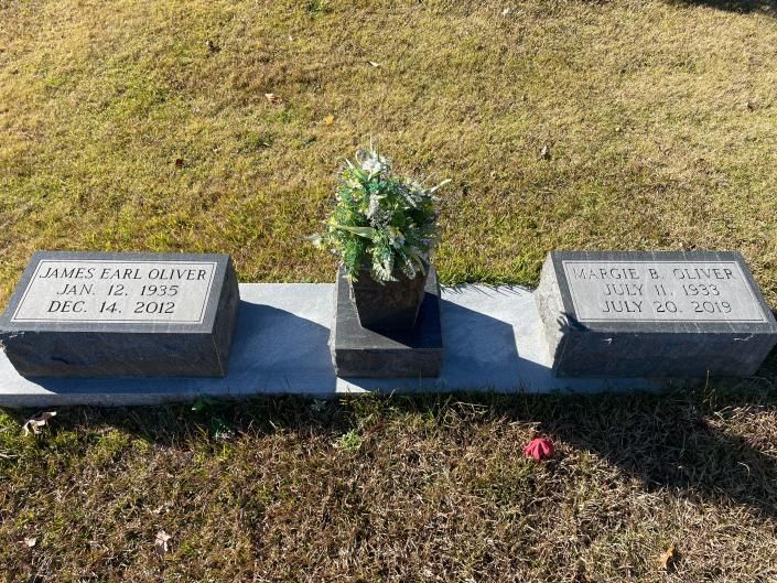 Two small headstones with a flower pot between them on a grassy grave site.