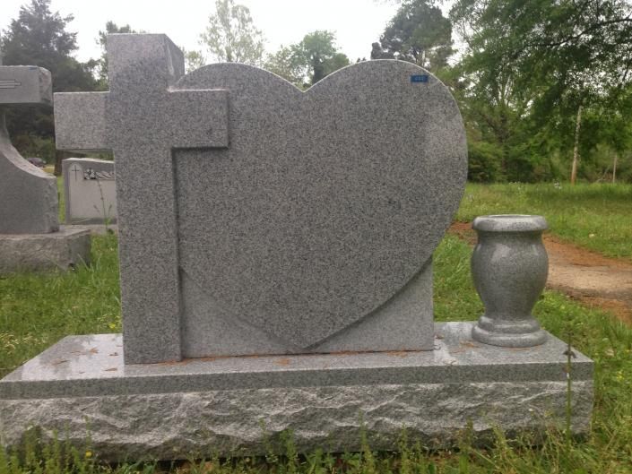 Gray granite heart-shaped gravestone with a cross, set on a stone base outdoors