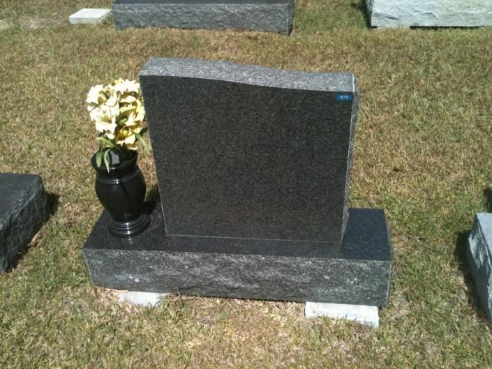 Gravestone with a vase of white flowers in a cemetery, set on grass.