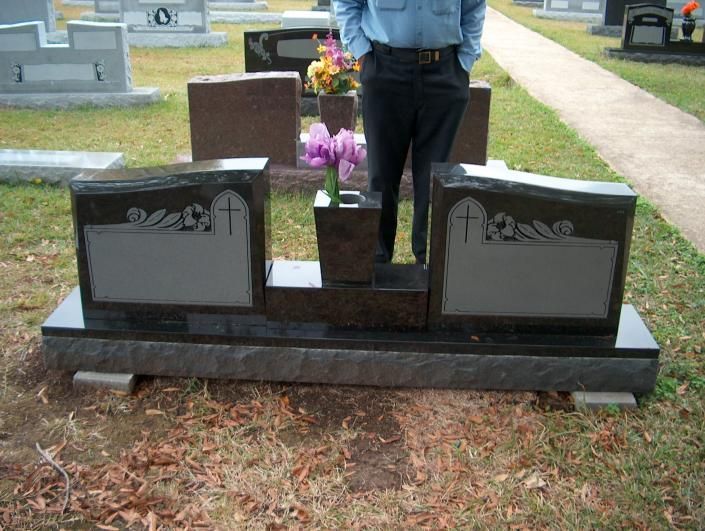 Person standing by a gravestone decorated with flowers in a cemetery