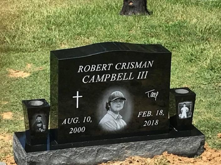 Black granite gravestone in grass, engraved “Robert Crisman Campbell III” with dates Aug. 10, 2000 and Feb. 18, 2018.