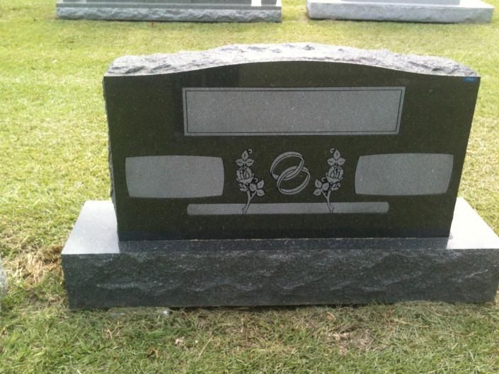 Black gravestone with engraved floral design on a grassy cemetery lawn.