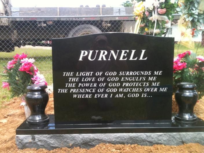 Black gravestone with white “PURNELL” lettering, flanked by pink flowers and vases in a cemetery