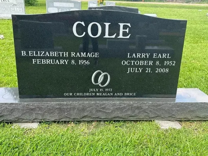 Black granite gravestone reading COLE with engraved names and dates in a grassy cemetery.
