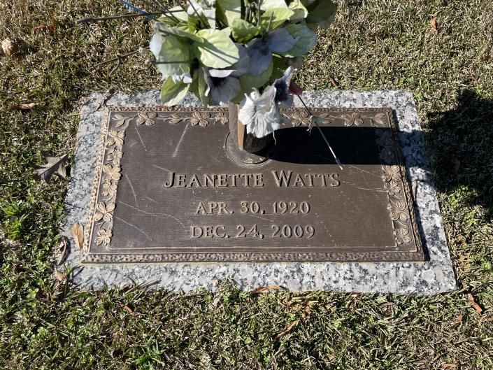 Gravestone with flowers, engraved “Jannette Wams,” in a grassy cemetery.