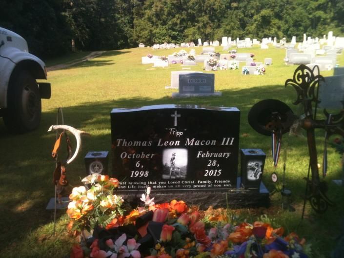 Memorial gravestone with flowers in a sunny cemetery, other headstones in the background