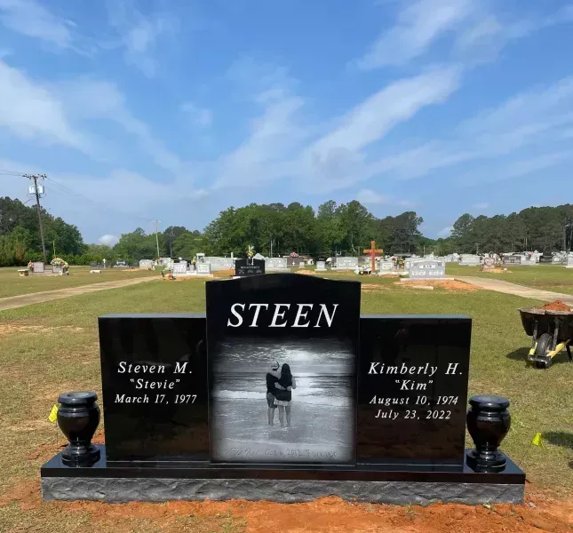 Black STEEN gravestone in a cemetery with two side inscriptions and a central portrait photo