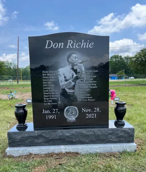 Memorial gravestone for Don Richie with portrait, names, and dates in a grassy cemetery under blue sky